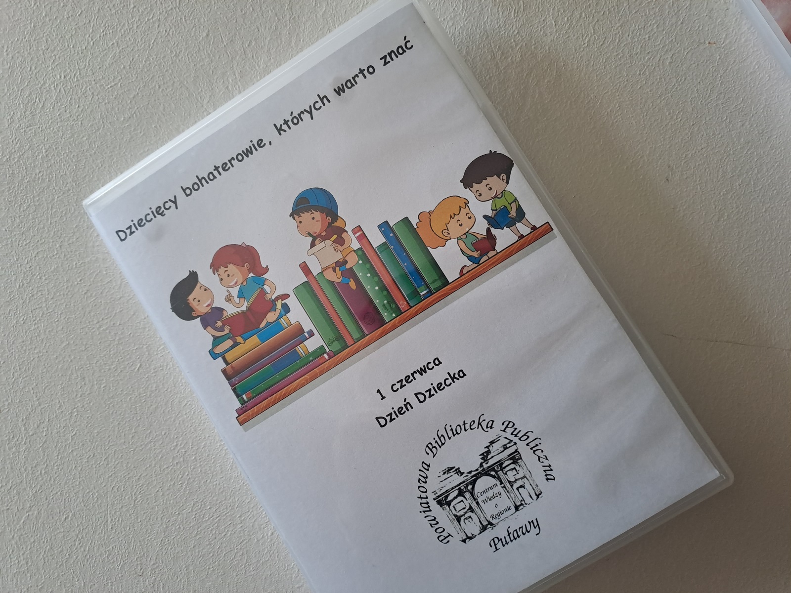 Zdjęcie prezentuje wystawę powieszoną na korytarzu przed biblioteką prezentującą różne okładki książek, w których bohaterami są dzieci. 