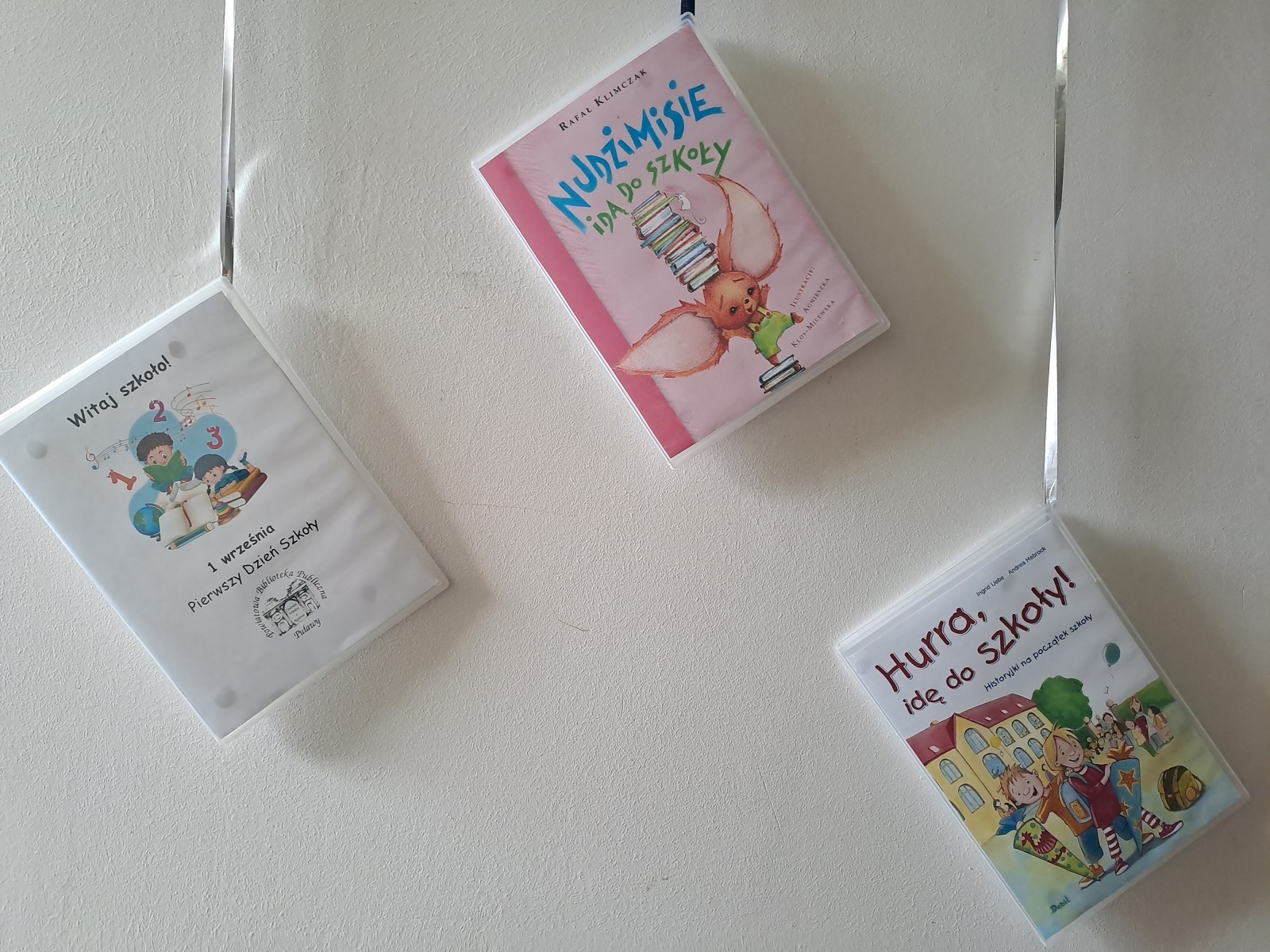 Zdjęcie prezentuje wystawę powieszoną na korytarzu przed biblioteką prezentującą różne okładki książek dla dzieci, w tytule których pojawia się wyraz szkoła. 