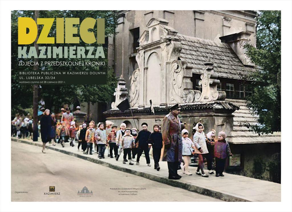 Zdjęcie to plakat wystawy pt. "Dzieci Kazimierza". Widać na nim przedszkolaki idące na spacer. W tle Kazimierski Ośrodek Kultury, Promocji i Turystyki.  