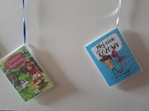 Zdjęcie prezentuje wystawę powieszoną na korytarzu przed biblioteką prezentującą różne okładki książek dla dzieci, w tytule których występuje nazwa jakiegoś koloru.  