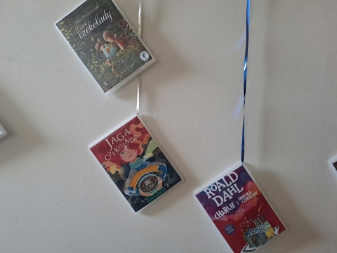 Zdjęcie prezentuje wystawę powieszoną na korytarzu przed biblioteką prezentującą różne okładki książek z wyrazem czekolada w tytule.