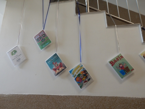 Zdjęcie prezentuje wystawę powieszoną na korytarzu przed biblioteką prezentującą różne okładki książek dla dzieci promujących ochronę środowiska i ekologiczne działania na rzecz naszej planety.