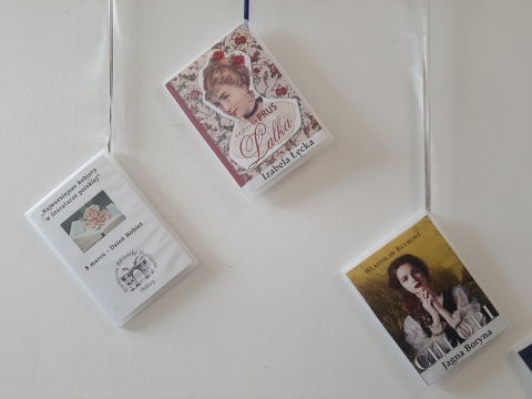 Zdjęcie prezentuje wystawę powieszoną na korytarzu przed biblioteką prezentującą różne okładki książek, w których ważna rolę odgrywają kobiety. 