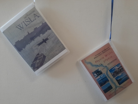 Zdjęcie prezentuje wystawę powieszoną na korytarzu przed biblioteką prezentującą różne okładki książek poświęconych rzece Wiśle. 