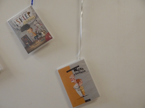 Zdjęcie prezentuje wystawę powieszoną na korytarzu przed biblioteką prezentującą różne okładki książek w których głównymi bohaterami są babcia i dziadek.