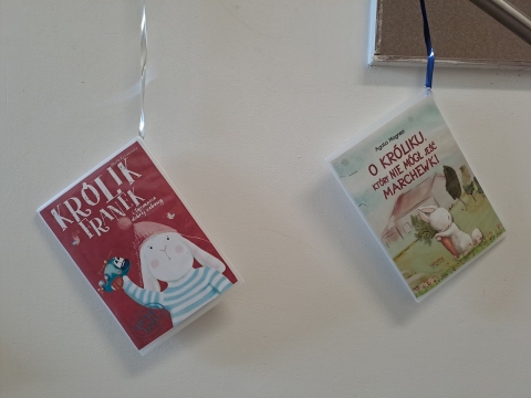 Zdjęcie prezentuje wystawę powieszoną na korytarzu przed biblioteką prezentującą różne okładki książek dla dzieci, w tytule których pojawia się wyraz królik.