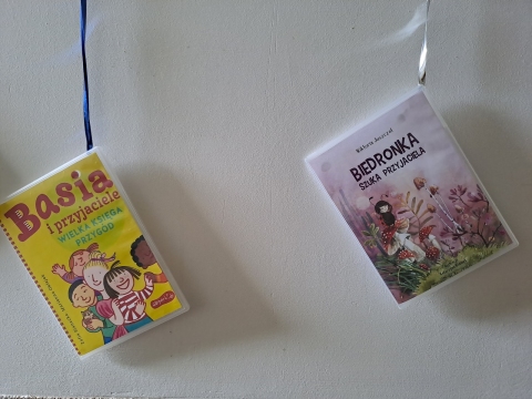 Zdjęcie prezentuje wystawę powieszoną na korytarzu przed biblioteką prezentującą różne okładki książek dla dzieci, w których głównym motywem jest przyjaźń.