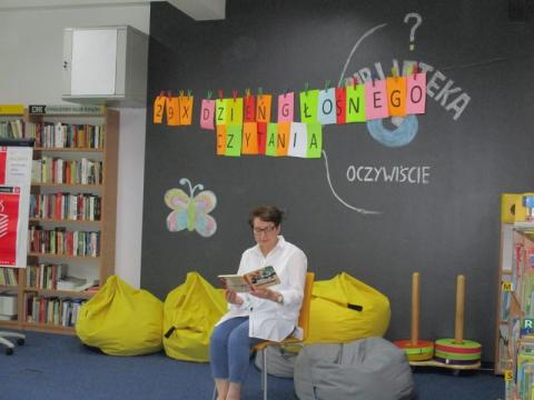 Zdjęcie prezentujące dzieci, uczestników Ogólnopolskiego Dnia Głośnego Czytania w bibliotece gminy Puławy. Pani bibliotekarka czyta przedszkolakom opowiadanie. 