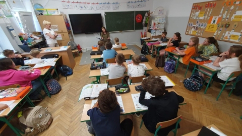 Zdjęcie prezentuje wspólne czytanie bajki „Wypożyczalnia skrzydeł. Opowieść o magii czytania” autorstwa Iwony Pietrzak-Płachty w Szkole Podstawowej nr 3 w Puławach. Na zdjęciu pani Katarzyna, dyrektor PBP w Puławach i uczniowie klasy 3.