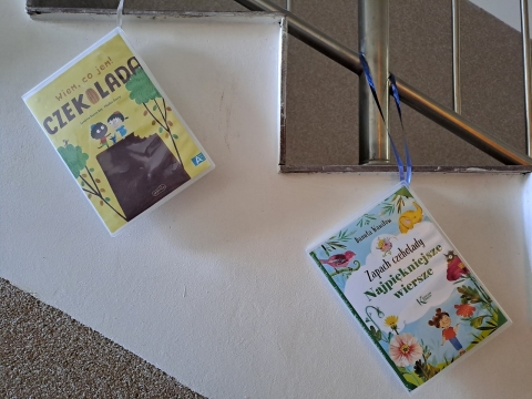 Zdjęcie prezentuje wystawę powieszoną na korytarzu przed biblioteką prezentującą różne okładki książek z wyrazem czekolada w tytule.