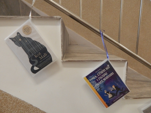 Zdjęcie prezentuje wystawę powieszoną na korytarzu przed biblioteką prezentującą różne okładki książek w których głównym bohaterem jest kot. 