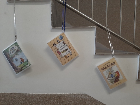 Zdjęcie prezentuje wystawę powieszoną na korytarzu przed biblioteką prezentującą różne okładki książek pt. „Kubuś Puchatek” 