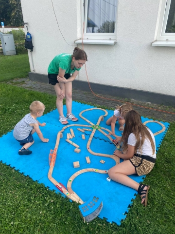 Zdjęcie przedstawia dzieci układające tory kolejowe i bawiące się pociągami. 