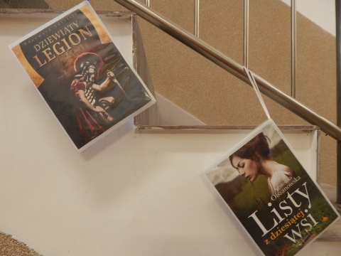 Zdjęcie prezentuje wystawę powieszoną na korytarzu przed biblioteką prezentującą różne okładki książek ze numerem tytule.