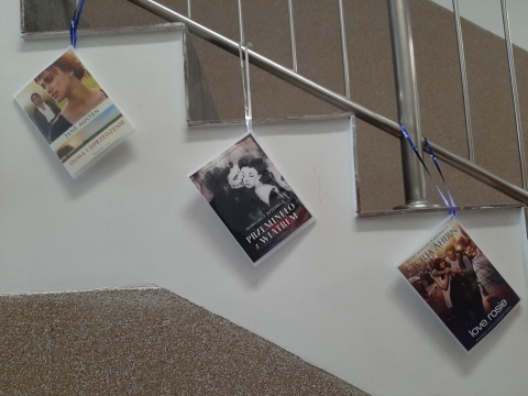 Zdjęcie prezentuje wystawę powieszoną na korytarzu przed biblioteką prezentującą różne okładki książek, których głównym tematem jest miłość. 