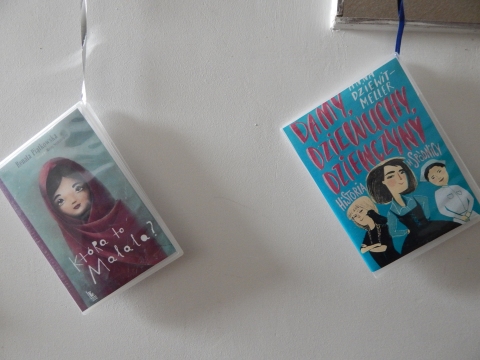 Zdjęcie prezentuje wystawę powieszoną na korytarzu przed biblioteką prezentującą różne okładki książek o inteligentnych, odważnych i silnych kobietach.