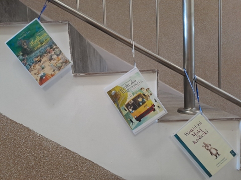 Zdjęcie prezentuje wystawę powieszoną na korytarzu przed biblioteką prezentującą różne okładki książek dla dzieci, w tytule których pojawia się wyraz królik.
