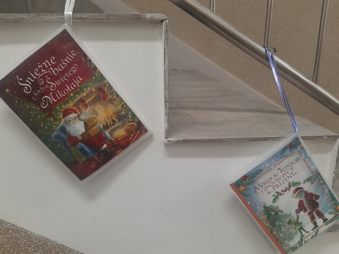 Zdjęcie prezentuje wystawę powieszoną na korytarzu przed biblioteką prezentującą różne okładki książek ze Świętym Mikołajem tytule.