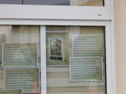 Zdjęcie prezentuje wystawę na oknach Powiatowej Biblioteki Publicznej w Puławach pokazującą różne publikacje dotyczące wybuchu i przebiegu Powstania Styczniowego.
