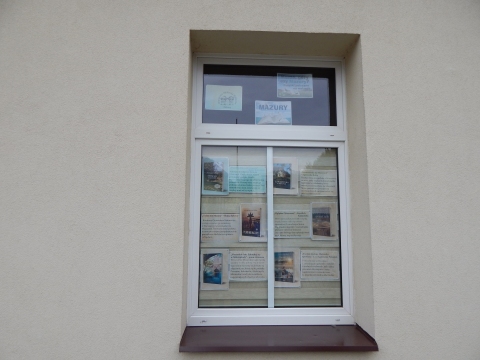 Zdjęcie prezentuje wystawę na oknach Powiatowej Biblioteki Publicznej w Puławach pokazującą książki, których akcja dzieje się nad morzem, w górach i na Mazurach.