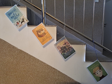 Zdjęcie prezentuje wystawę powieszoną na korytarzu przed biblioteką prezentującą różne okładki książek dla dzieci, w tytule których występuje nazwa jakiegoś koloru.  
