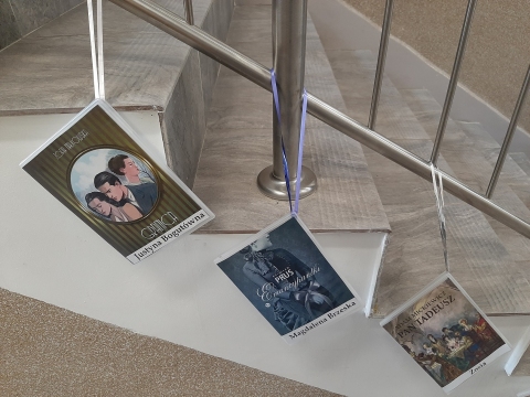 Zdjęcie prezentuje wystawę powieszoną na korytarzu przed biblioteką prezentującą różne okładki książek, w których ważna rolę odgrywają kobiety. 