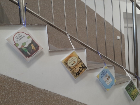 Zdjęcie prezentuje wystawę powieszoną na korytarzu przed biblioteką prezentującą różne okładki książek pt. „Kubuś Puchatek” 