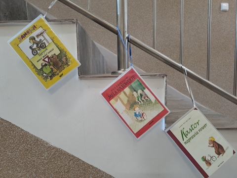 Zdjęcie prezentuje wystawę powieszoną na korytarzu przed biblioteką prezentującą różne okładki książek dla dzieci, w których ważnym punktem jest jazda na rowerze.  