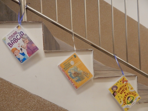 Zdjęcie prezentuje wystawę powieszoną na korytarzu przed biblioteką prezentującą różne okładki książek w których głównymi bohaterami są babcia i dziadek.