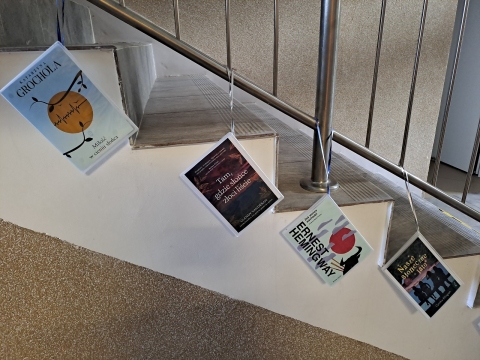 Zdjęcie prezentuje wystawę powieszoną na korytarzu przed biblioteką prezentującą różne okładki książek z wyrazem słońce w tytule.