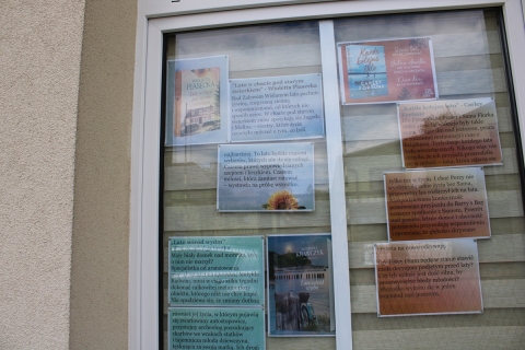 Zdjęcie prezentuje wystawę pt. „Książki z latem w tle” na oknach Powiatowej Biblioteki Publicznej, która prezentuje książki, których akcja rozgrywa się latem, a wakacyjne miesiące stanowią tło opowiadanych historii.