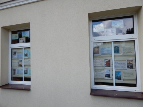Zdjęcie prezentuje wystawę na oknach Powiatowej Biblioteki Publicznej w Puławach pokazującą książki, których akcja dzieje się nad morzem, w górach i na Mazurach.