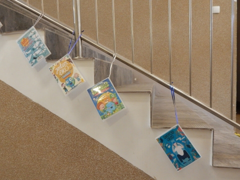 Zdjęcie prezentuje wystawę powieszoną na korytarzu przed biblioteką prezentującą różne okładki książek dla dzieci promujących ochronę środowiska i ekologiczne działania na rzecz naszej planety.