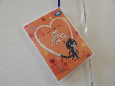 Zdjęcie prezentuje wystawę powieszoną na korytarzu przed biblioteką prezentującą różne okładki książek w których głównym bohaterem jest kot. 