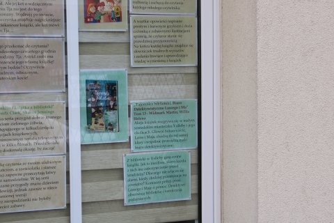 Zdjęcie prezentuje wystawę na oknach Powiatowej Biblioteki Publicznej pokazującą książki dla dzieci, których akcja rozgrywa się właśnie w bibliotece. 