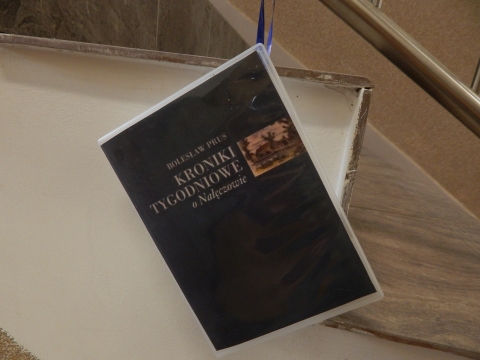 Zdjęcie prezentuje wystawę powieszoną na korytarzu przed biblioteką prezentującą różne okładki książek autorstwa Bolesława Prusa. 