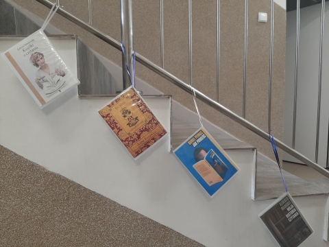 Zdjęcie prezentuje wystawę powieszoną na korytarzu przed biblioteką prezentującą różne okładki książek, w których to właśnie książka jest głównym bohaterem. 