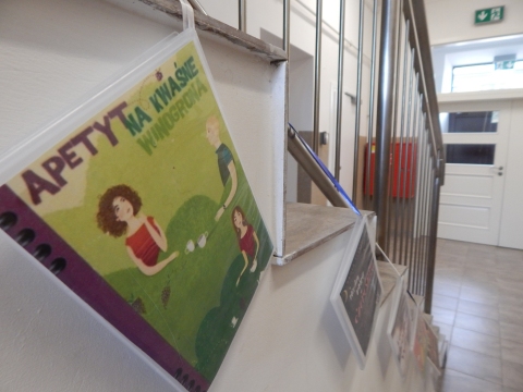 Zdjęcie prezentuje wystawę powieszoną na korytarzu przed biblioteką prezentującą różne okładki książek ze smakiem owoców  tytule.