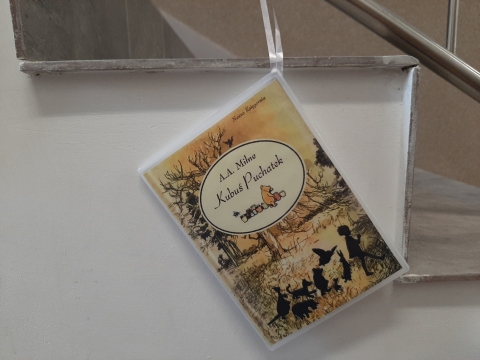 Zdjęcie prezentuje wystawę powieszoną na korytarzu przed biblioteką prezentującą różne okładki książek pt. „Kubuś Puchatek” 