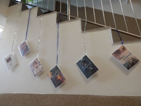 Zdjęcie prezentuje wystawę powieszoną na korytarzu przed biblioteką prezentującą różne okładki książek autorstwa Bolesława Prusa. 