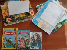 Zdjęcie przedstawia ułożone na stoliku książki autorstwa Marii Konopnickiej i pierwsze prace, które wpłynęły na konkurs plastyczny pt. „Z wizytą w bajkowym świecie Marii Konopnickiej”.